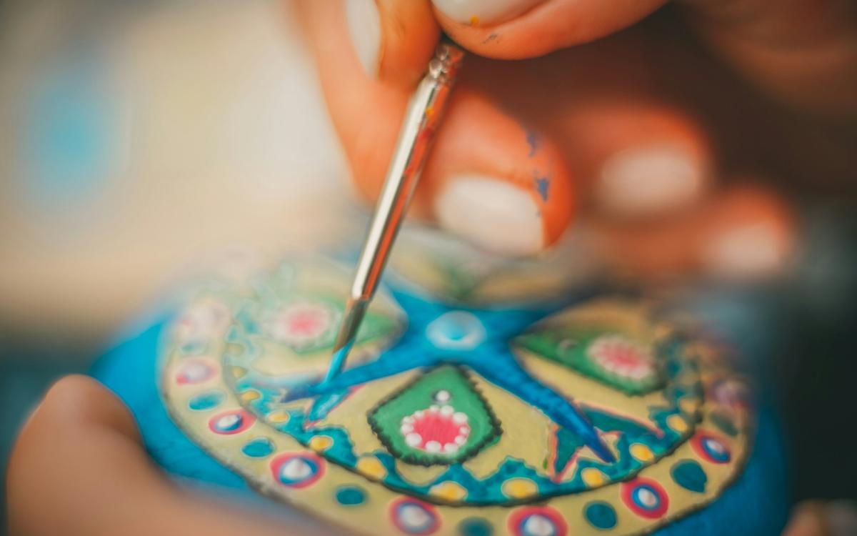 Mână care pictează cu o pensulă fină un ornament rotund