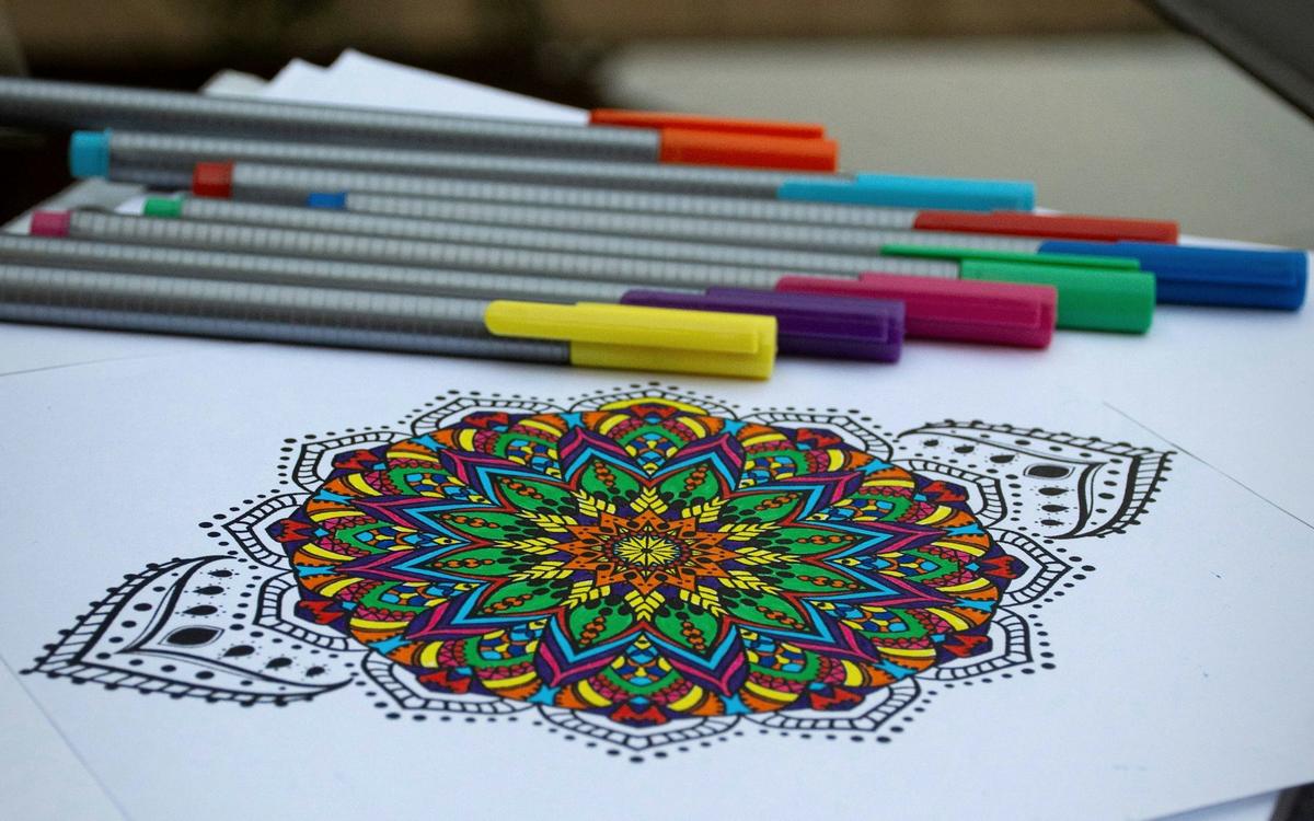 Mandală colorată cu markere, lângă un set de linere colorate