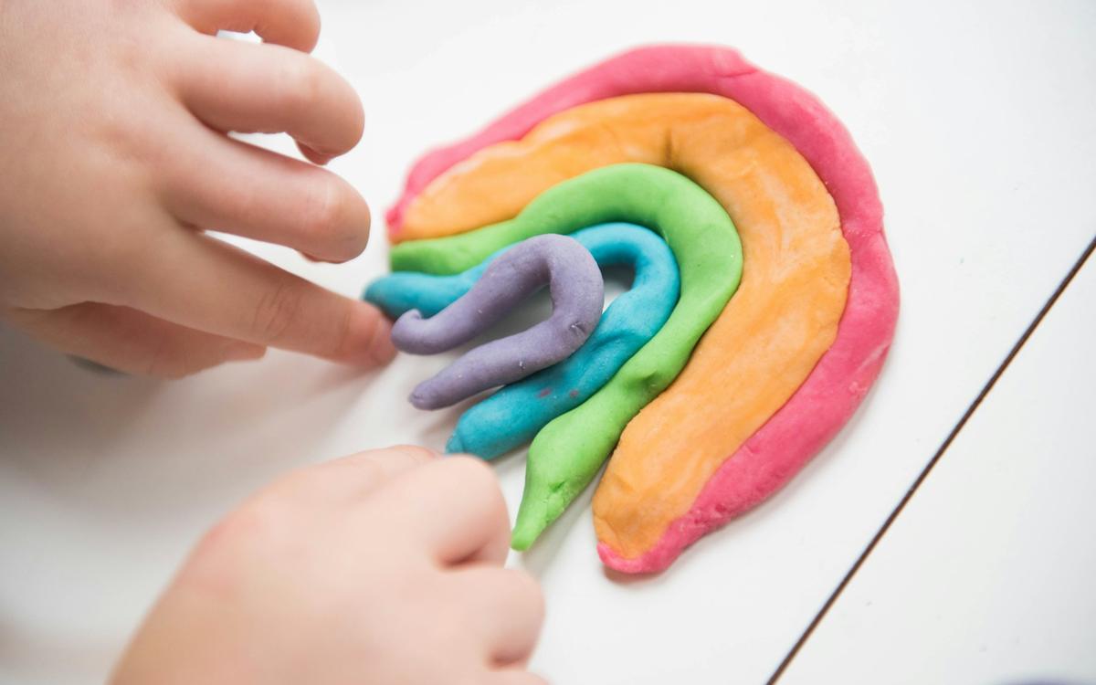 Mâini de copil care modelează un curcubeu din plastilină colorată
