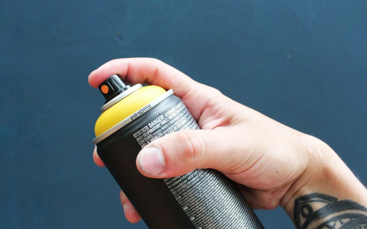 Mână care ține un tub de spray cu capac galben