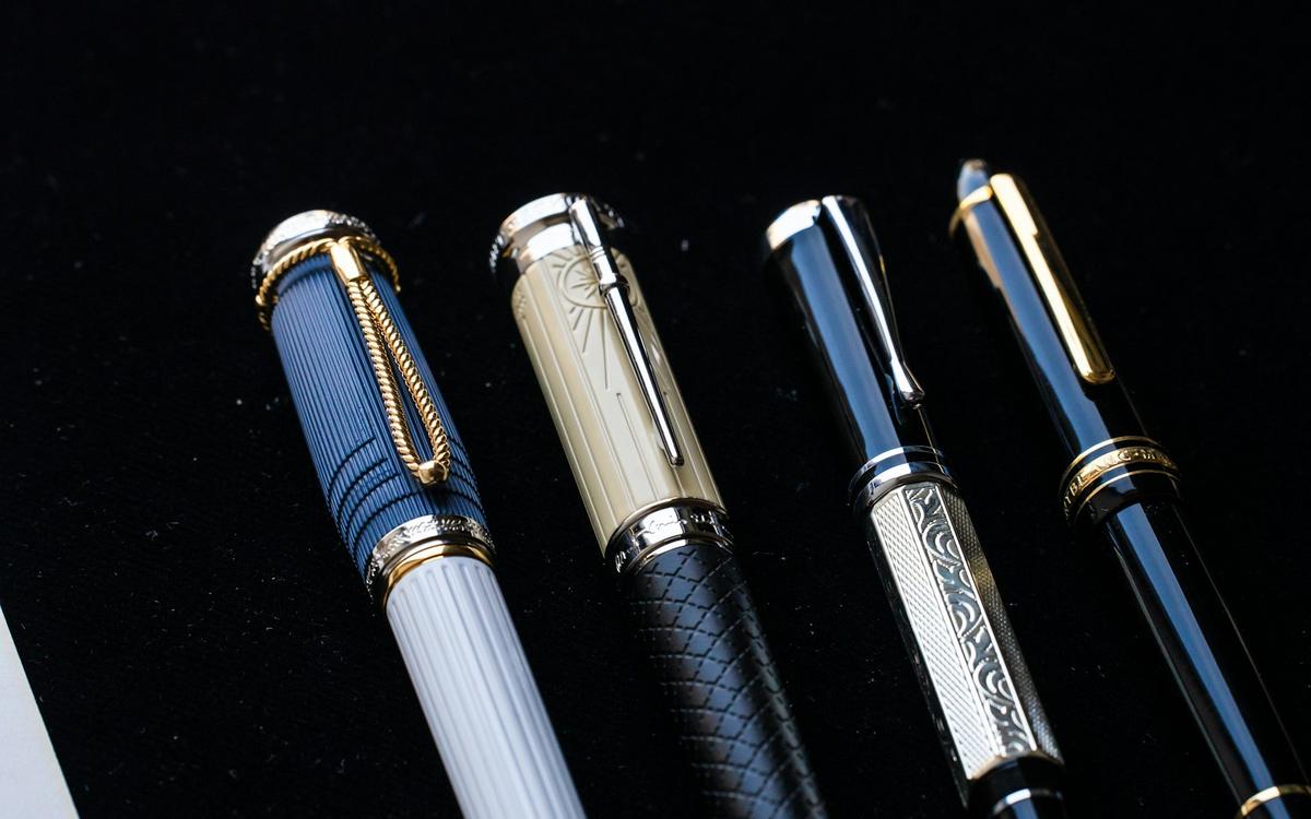 Patru stilouri elegante, cu capace metalice, pe fundal negru